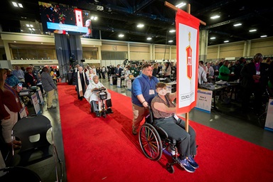 Sara Martin, her wheelchair pushed by Dan Levine, carries the banner of the Council of Bishops into the opening worship service of the United Methodist General Conference in Charlotte, N.C., on April 23. Behind them comes a procession of United Methodist bishops, headed by Bishop Forrest Stith on a motorized wheelchair. Photo by Paul Jeffrey, UM News. Sara Martin, her wheelchair pushed by Dan Levine, carries the banner of the Council of Bishops into the opening worship service of the United Methodist General Conference in Charlotte, N.C., on April 23. Behind them comes a procession of United Methodist bishops, headed by Bishop Forrest Stith on a motorized wheelchair. Photo by Paul Jeffrey, UM News.