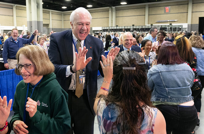 El Obispo Thomas J. Bickerton choca los cinco con delegados/as, visitantes y personal de la Conferencia General Metodista Unida reunida en Charlotte, Carolina del Norte, que bailan en los pasillos después del culto matutino del último día de la conferencia. Detrás de él está el Obispo John Schol. Foto de Mike DuBose, Noticias MU.