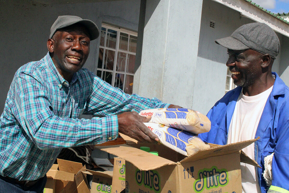 Sinoia Nyamukapa, a teacher at Nyadire High School, hands food to Tobias Gombera, farm supervisor for the school, at Nyadire Mission in Mutoko, Zimbabwe. The Nyadire Connection, a faith-based nonprofit founded by United Methodists, raised money to provide food for hundreds of families at the mission through the end of the year. Photo by Kudzai Chingwe, UM News.
