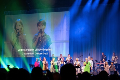 Los hermanos Agnes y Alfred Quint, en la pantalla, se unen a cantantes de la Iglesia Unida de Suecia para dirigir a los/as fieles en “O Store Gud”, el nombre original sueco del himno que los/as angloparlantes conocen como “Cuán Grande es Él”, durante la Conferencia Metodista Mundial. Celebrada en Gotemburgo, Suecia. Foto de Klaus Ulrich Ruof, Conferencia Central de Alemania. Los hermanos Agnes y Alfred Quint, en la pantalla, se unen a cantantes de la Iglesia Unida de Suecia para dirigir a los/as fieles en “O Store Gud”, el nombre original sueco del himno que los/as angloparlantes conocen como “Cuán Grande es Él”, durante la Conferencia Metodista Mundial. Celebrada en Gotemburgo, Suecia. Foto de Klaus Ulrich Ruof, Conferencia Central de Alemania.