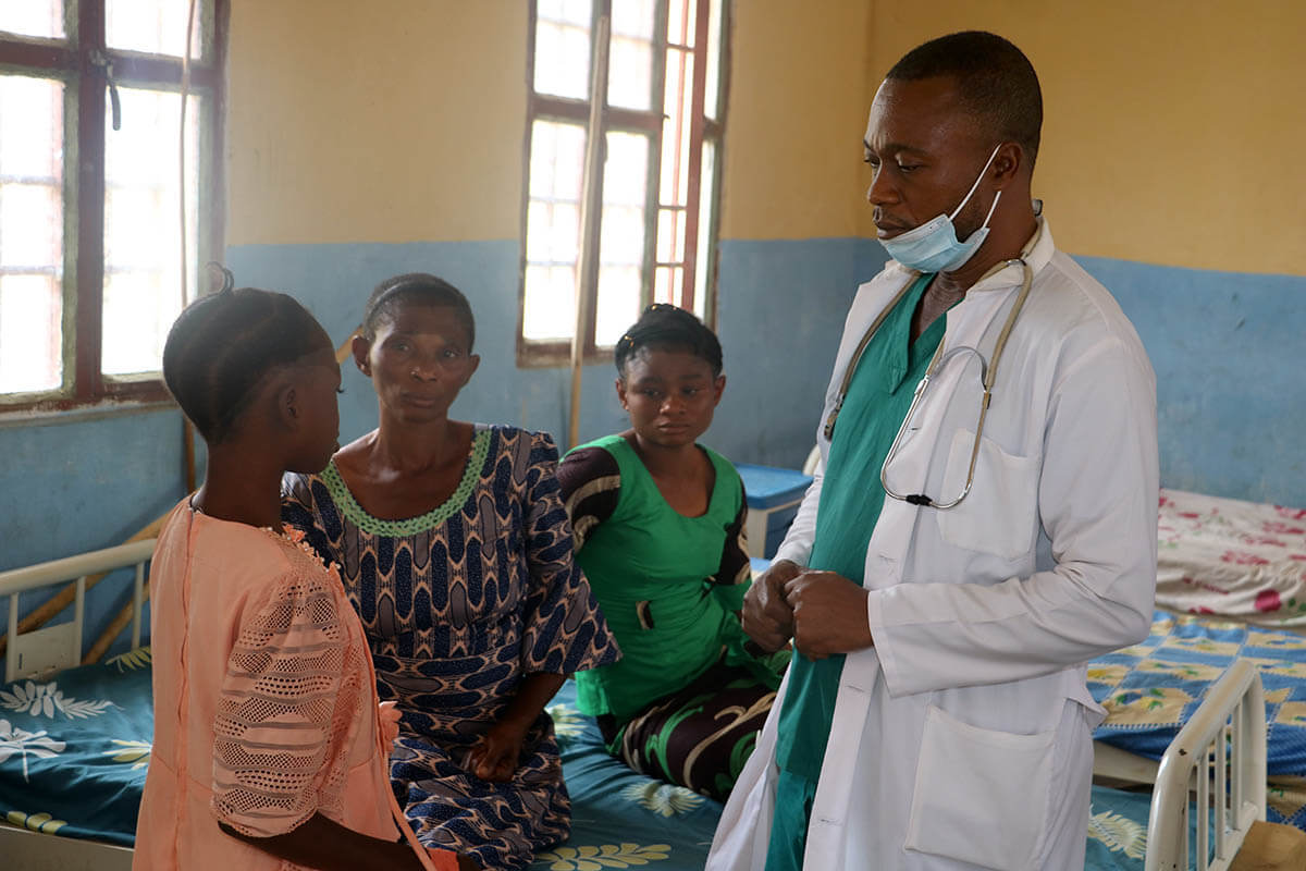 O Dr. Pierre Omesombo, médico assistente do Hospital Geral de Tunda, fala com um doente em Tunda, no Congo. O país é o epicentro de um surto de varíola, responsável por 96% de todos os casos, informa o CDC de África. A instalação médica Metodista Unida tem um laboratório que permite o diagnóstico rápido da varíola e a monitorização eficaz do surto. Foto de Chadrack Tambwe Londe, Notícias MU.