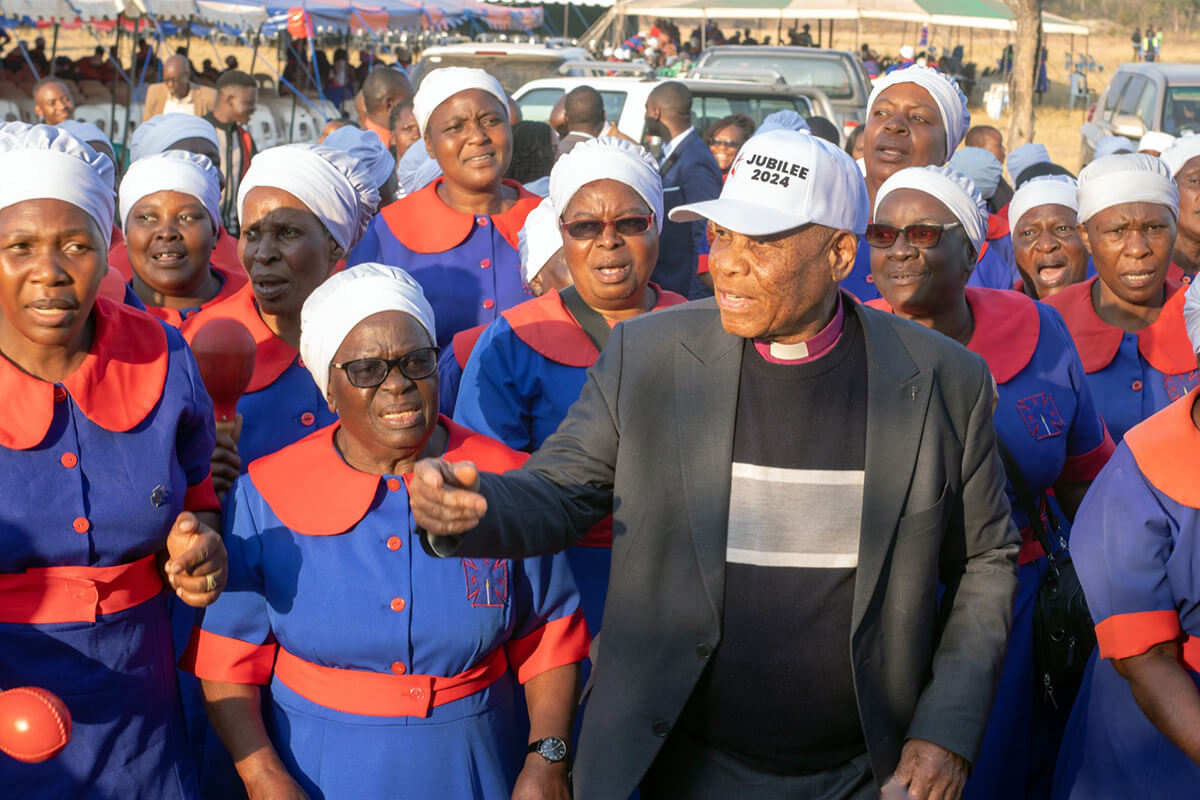Bishop Eben K. Nhiwatiwa and his wife, Greater Nhiwatiwa (to bishop's right), attend Jubilee 2024 at a campground in Darwendale, Zimbabwe. The convention was one of two jubilee events that drew some 20,000 church members from the Zimbabwe Episcopal Area on Aug. 8-11. Many in attendance were members of Rukwadzano Rwe Wadzimai, the women’s organization, who were dressed in their signature red and blue uniforms. Photo by Tarisai Mubaiwa. 