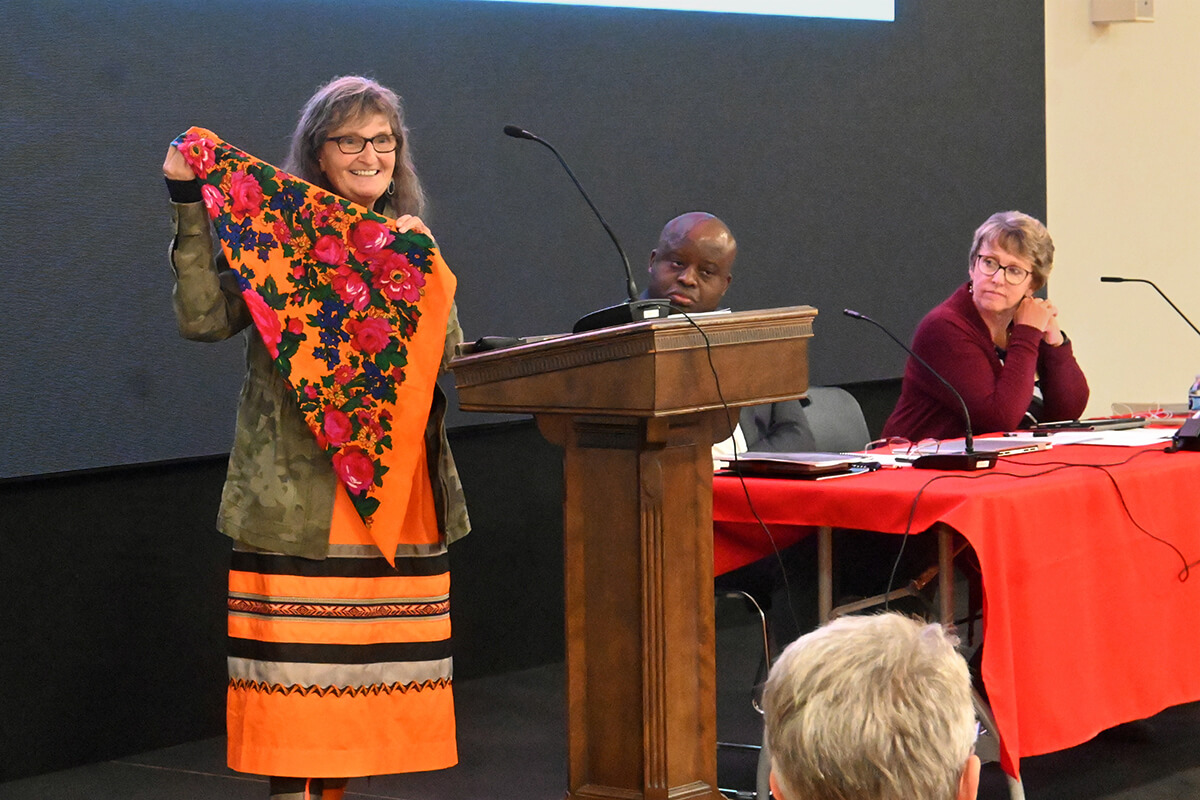 Ragghi Rain Calentine (à esquerda), um membro da Mesa Conexional e presidente do Grupo Internacional de Nativos Americanos da Igreja Metodista Unida, exibe um lenço Noohkom durante a reunião da Mesa Conexional de 24 a 27 de Outubro em Dallas. As mulheres Nativo-Americanas transportam os lenços para se lembrarem que as suas avós estão sempre a caminhar com elas, especialmente durante os tempos difíceis. Também na foto estão o Bispo da Área de Katanga Norte, Mande Muyombo, presidente da Mesa Conexional, e Judi Kenaston, a principal oficial conexional do orgao de liderança. Foto de Jim Patterson, Notícias da MU.