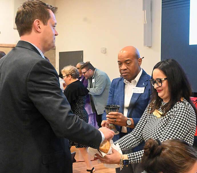 O Rev. Edlen Cowey (ao centro), pastor sénior da Igreja Metodista Unida Munger em Dallas, ajuda a servir a Sagrada Comunhão no dia 24 de Outubro durante a formação de orientação para os membros da Mesa Conexional, assistido por Gisele Seixas (à direita), gestora de operações e assistente executiva da Mesa Conexional. Foto de Jim Patterson, Notícias da MU.