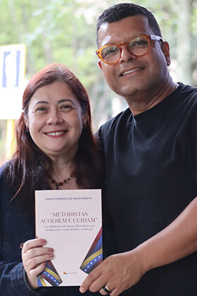 Eizel Ladeia y Fábio Fonseca posan con el libro "Metodistas Acogen y Cuidan" en un evento de lanzamiento de la publicación. Foto de Sara de Paula para Noticias MU.