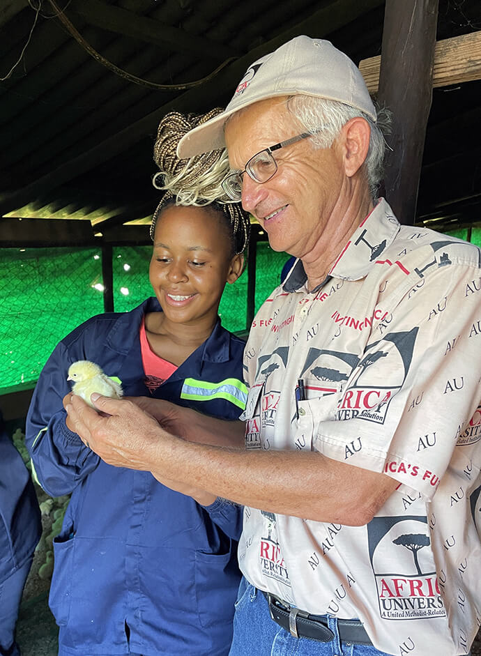 Le missionnaire Larry Kies et Audrey, étudiante à Africa University, admirent un poussin d'un jour à la ferme des rêves de l'école, où M. Kies a été chargé de cours et conseiller technique. Photo avec l'aimable autorisation de Larry Kies.