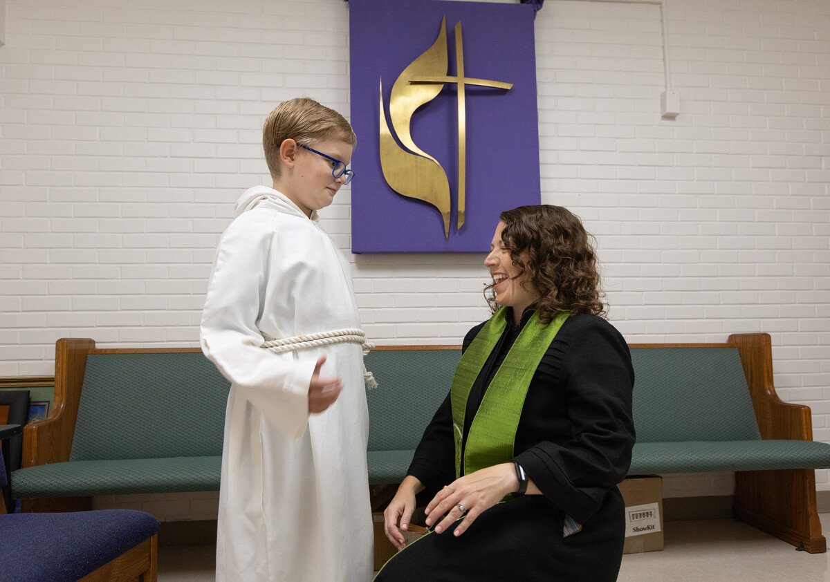The Rev. Colleen Bookter shares a laugh with acolyte Anderson Meyer while helping him get fitted with a robe at St. Luke’s United Methodist Church. The cross and flame on the wall behind them was salvaged from the sanctuary following Hurricane Katrina. Photo by Mike DuBose, UM News.