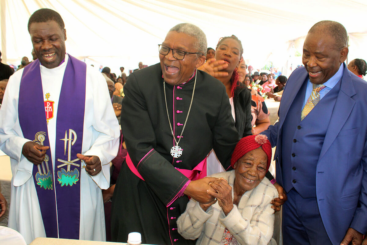 Ethiopian Episcopal Church Bishop Malusi Mpumlwana (in black) congratulates 102-year-old Janet Gowe (seated) on the realization of her decades-long dream for a United Methodist church in her farm community of Murewa, Zimbabwe. United Methodist Bishop Gift K. Machinga (left) led the dedication of Hoyuyu United Methodist Church’s Nzira Sanctuary on May 25. At right is Kingston Kajese, Gowe’s son, who spearheaded the construction of the sanctuary. Photo by Kudzai Chingwe, UM News.