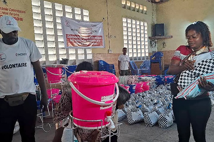 Joël Paradis, un volontaire du Bureau de Gestion des Catastrophes de l’UMCOR dans la Région Épiscopale du Congo Central, débout lors de l’opération de distribution à côté d’une bénéficiaire de l’aide des méthodistes unis. Des volontaires, parfois eux-mêmes touchés, ont bravé des routes impraticables pour acheminer l’aide, utilisant pirogues artisanales et portage manuel pour atteindre les zones isolées. Photo du Révérend Pasteur Fiston Okito, UM News. Joël Paradis, un volontaire du Bureau de Gestion des Catastrophes de l’UMCOR dans la Région Épiscopale du Congo Central, débout lors de l’opération de distribution à côté d’une bénéficiaire de l’aide des méthodistes unis. Des volontaires, parfois eux-mêmes touchés, ont bravé des routes impraticables pour acheminer l’aide, utilisant pirogues artisanales et portage manuel pour atteindre les zones isolées. Photo du Révérend Pasteur Fiston Okito, UM News.