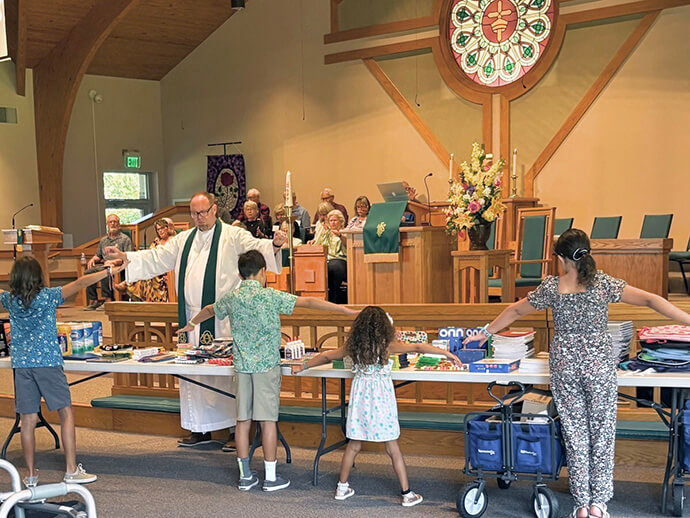 The Rev. Jesse Baker prays over children during worship at First United Methodist Church of Elon, N.C. Baker writes poetry to put Scripture in perspective, which he says helps him write more compelling sermons. Photo courtesy of First United Methodist Church.
