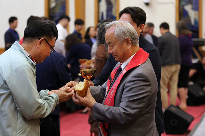 Bishop Hee-Soo Jung serves bread to the Rev. Chansoon Lim, pastor of Covenant United Methodist Church in Arlington, Texas, during Holy Communion at the opening worship of the Korean Association of The United Methodist Church. Photo by the Rev. Thomas E. Kim, UM News.