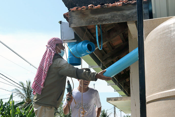 A WASH Academy participant and a local worker connect gutters to rainwater-harvesting tanks designed to convert rainwater into drinking water on Oct. 15 at Hun Sen Sa’ng High School in Phnom Penh, Cambodia. During the church-supported academy, students learned about clean water and systems to improve access. Photo by the Rev. Thomas E. Kim, UM News.