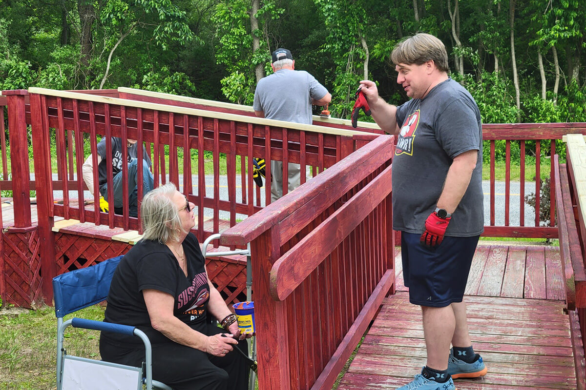 Lisa Bowser (left), lay leader of Marshallton United Methodist Church in West Chester, Pa., speaks with Christian Boehnke as church members Neal Bowser and Jonah Eckert work in the background to renovate a disability access ramp at St. John United Methodist Church in Bridgeton, N.J. St. John is the fifth-oldest historically Native American church in the denomination. The two congregations have been sharing in ministry and fellowship since 2024 as part of Marshallton’s efforts to address racial injustice toward Indigenous people its area. Photo by David Eckert.