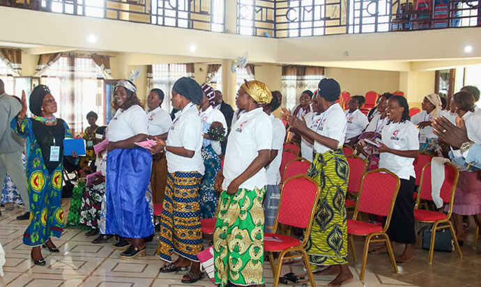 Wives of pastors and district superintendents from eastern Congo, wearing T-shirts bearing the logo of the United Methodist Board of Global Ministries, stand and applaud during a training session in Kindu, Congo. More than 60 women participated in the leadership development program in February. Photo by Chadrack Tambwe Londe, UM News.