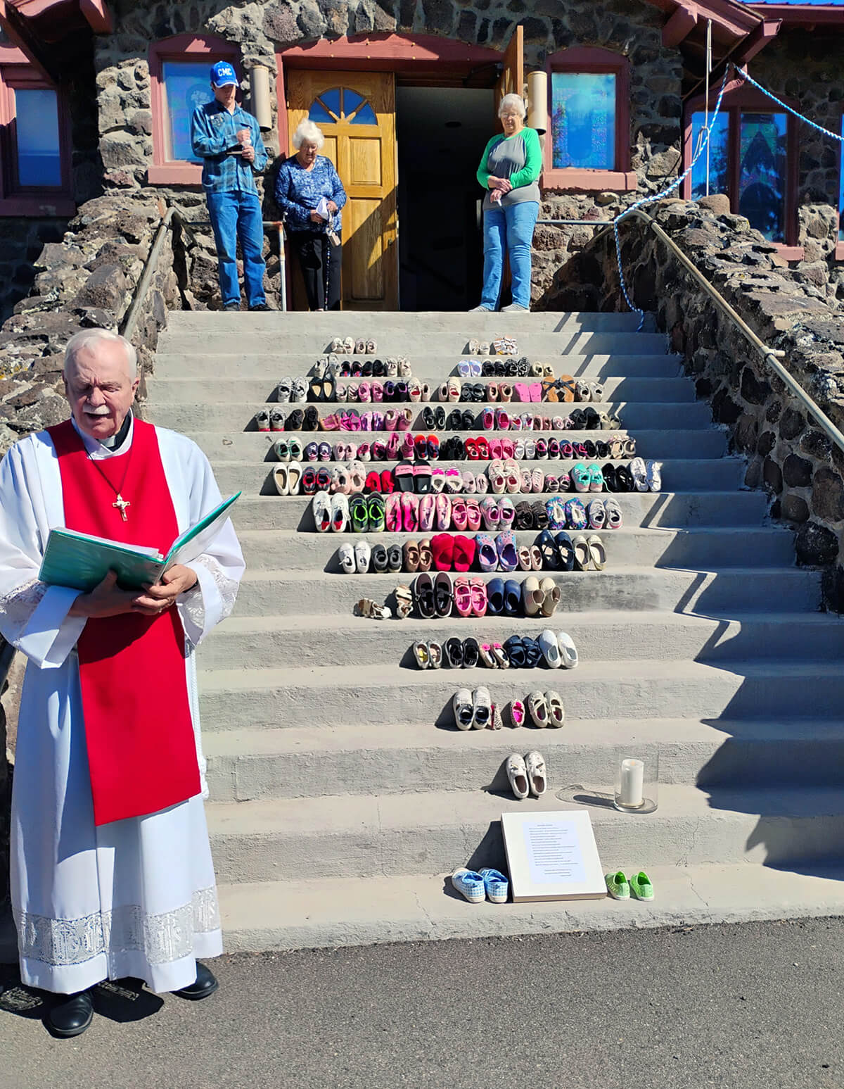 The Rev. Bob Anders (at left) leads a time of prayer on April 3, Good Friday at Cedaredge Community United Methodist Church in Cedaredge, Colo. The church displayed on its steps a memorial showing pairs of shoes to represent the 168 children and teachers killed Feb. 28 in the bombing of the girls’ school in Minab, Iran. Photos of the memorial went viral on social media. Amid the tenuous ceasefire, United Methodists continue to speak out against the war and especially threats of genocide. Photo courtesy of Anders, Cedaredge Community United Methodist Church. 
