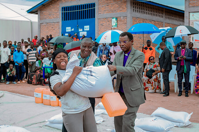 Bishop Emmanuel Sinzohagera of Burundi (right) and Global Missionary Abro Patrick (center) help a displaced person carry a bag of food at the Musenyi camp in Burundi. The United Methodist Church, with support from UMCOR, has provided humanitarian aid and other support to more than 22,000 refugees from Congo living at the camp. Photo courtesy of the communications department of the Burundi-Rwanda Episcopal Area.
