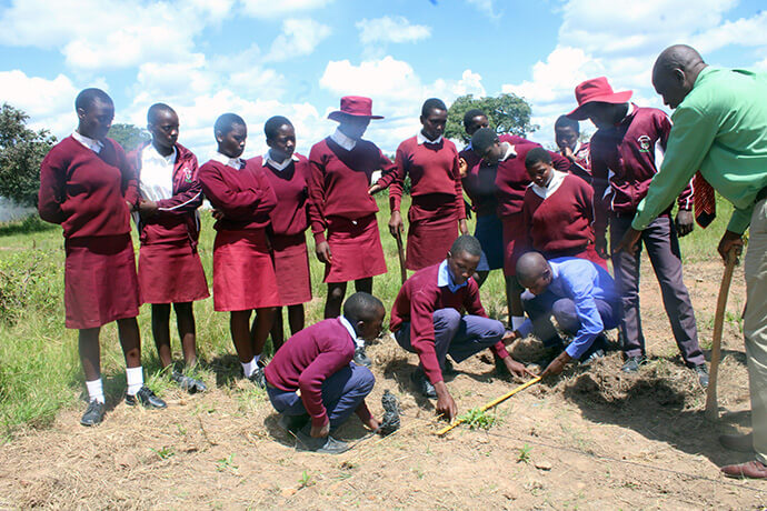 Tichaona Cornelius Dzvinamurungu guide les élèves tandis qu'ils mesurent des plantes à l'école secondaire Hanwa Mission. Dans le cadre de l'initiative de plantation d'arbres lancée par l'Église, les élèves mettent en pratique leurs compétences en mathématiques et s'initient au traitement et à l'analyse des données. Photo de Kudzai Chingwe, UM News.