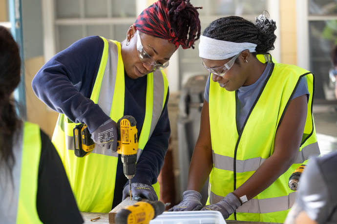 Kenisha Thomas (left) and Gnyia McDonald practice using an electric drill to drive screws at the Women in Construction program in Biloxi, Miss. 