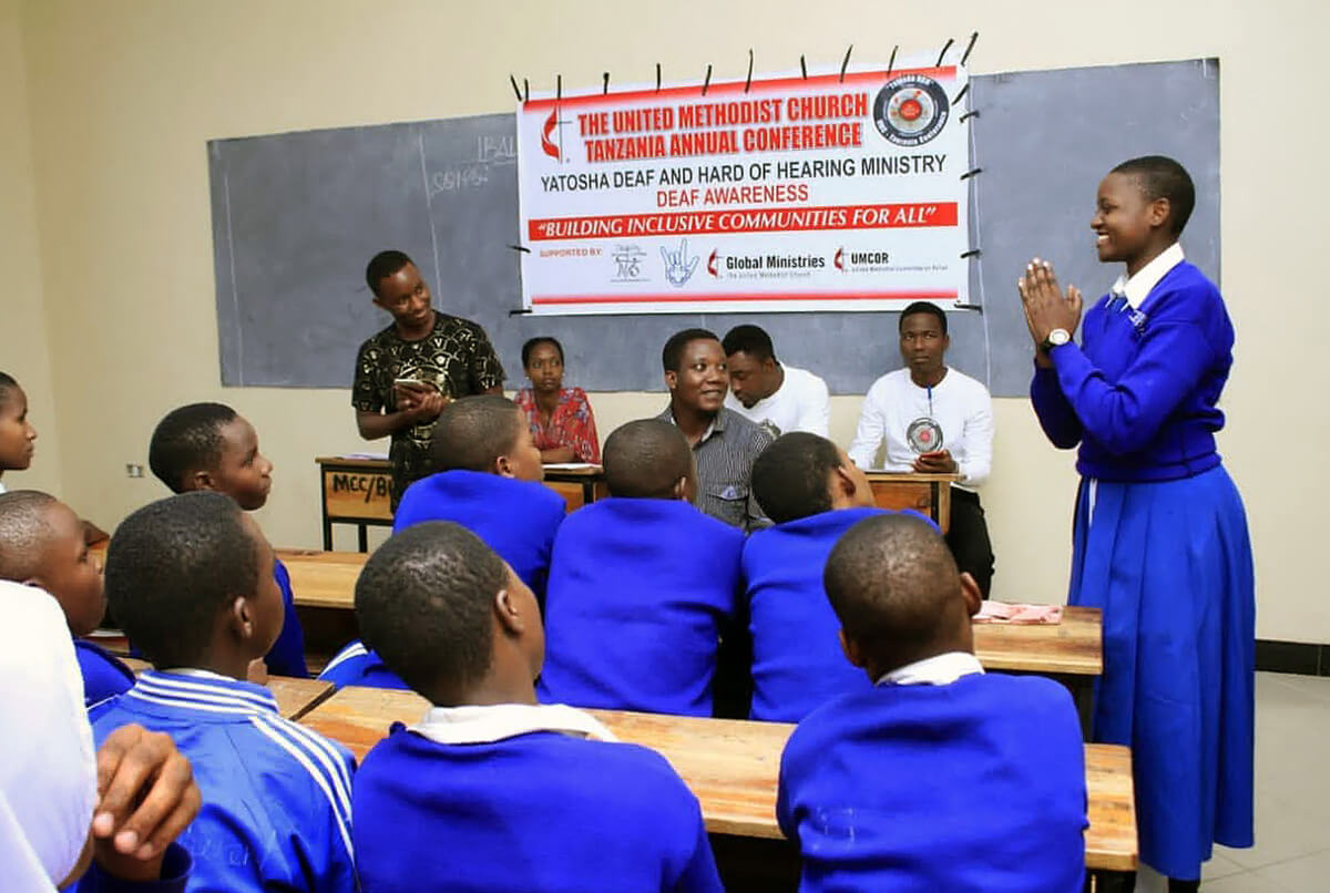 A student signs for her classmates as Michael Pius (standing in black shirt), a United Methodist health officer, provides information to Deaf students at Buhongwa Secondary School in Mwanza, Tanzania, in 2021. Part of the Tanzania Conference’s Yatosha Deaf Ministry, the outreach includes spiritual guidance and teaching practical skills that empower Deaf students to live healthier and more fulfilling lives. File photo by Robert Aloyce, UM News.
