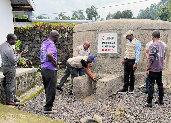 Dr. Damas Lushima washes his hands at the faucet of a rainwater cistern as other members of the humanitarian team look on in the village of Kibumba in North Kivu, Congo. Direct access to clean water helps promote basic hygiene practices and combats the spread of waterborne diseases among vulnerable families in the region. Photo by Jolie Shabani, UM News.