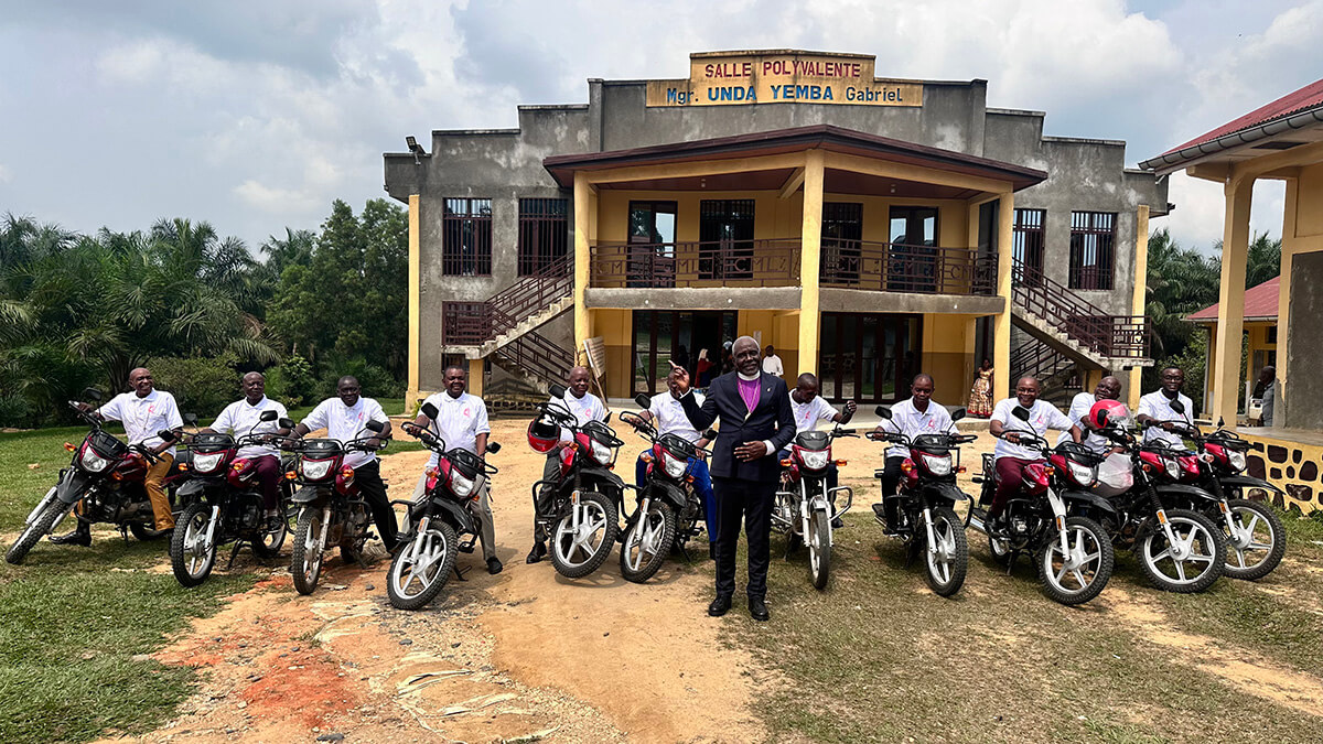 Bishop Antoine Tambwe Kalema (center) poses for a photo with the 11 district superintendents from the Eastern Congo Conference who received new motorcycles as a gift from the bishop during the 2026 annual conference. Many of the church leaders had spent years traveling on foot or by bicycle to minister to their communities. Behind them is the Mgr. Gabriel Unda Yemba Multipurpose Hall at the Mama Lynn Center in Kindu, Congo. Photo by Chadrack Tambwe Londe, UM News.