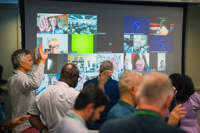 Corey Schlosser-Hall (left), deputy executive for vision, innovation and rebuilding at the Presbyterian Church (U.S.A.), prays along with online and in-person attendees. Photo by Chris Law, Discipleship Ministries.