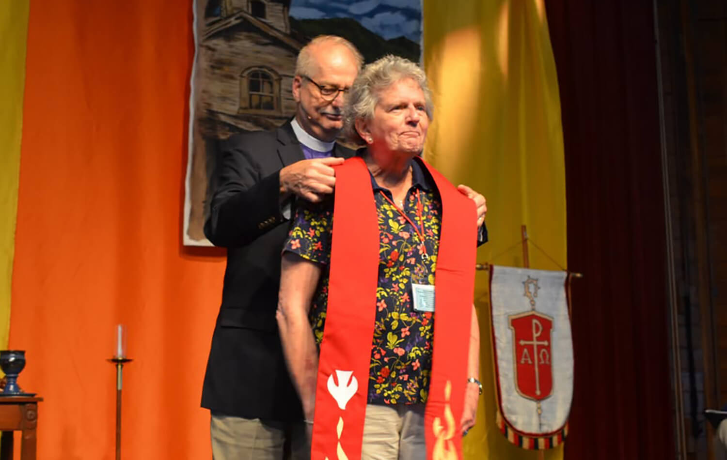 Obispo Ken Carter, actual líder episcopal de la Conferencia Anual del Oeste de Carolina del Norte, impone la estola a la Revda. Lauren Grace Scruggs como símbolo restitución de sus credenciales ministeriales después de 32 años de haberlas entregados a solicitud de su obispo por su orientación sexual. Foto cortesia de la Conferencia Anual del Oeste de Carolina del Norte.