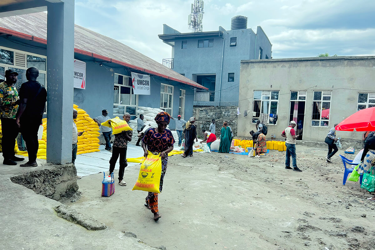Une bénéficiaire quitte le point de distribution en portant son sac de vivres fourni par l’UMCOR et le Bureau de gestion des catastrophes de la Région épiscopale de l’Est du Congo à Goma. Face au chômage et à la perte des terres agricoles causée par la guerre, l’aide alimentaire apporte un soulagement essentiel aux familles en difficulté. Photo : Jolie Shabani Mulebinge, UM News.