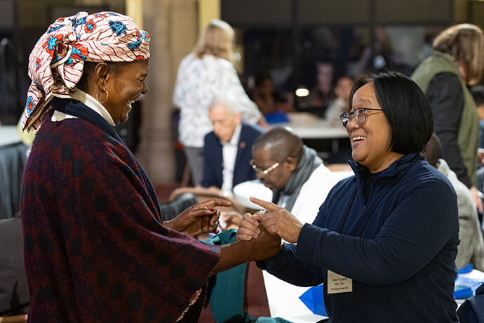 The Rev. Eunice Iliya (left) and Karen Prudente greet one another during the opening session of the United Methodist Leadership Gathering at Knox United Church in Calgary, Canada. Iliya is with The United Methodist Church of Nigeria and Prudente is vice chair of the National Federation of Asian American United Methodists. Photo by Mike DuBose, UM News.